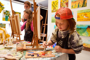 Een jongen met een oranje petje is aan het schilderen in het atelier van het Van Gogh Museum. Op de achtergrond een meisje en de workshopdocente. Foto: Suzanne Karsters
