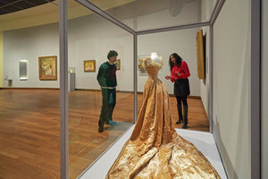 Twee bezoekers in de tentoonstelling 'Geel. Meer dan Van Goghs lievelingskleur' kijken naar de baljurk van geel fluweel. Foto: Michael Floor