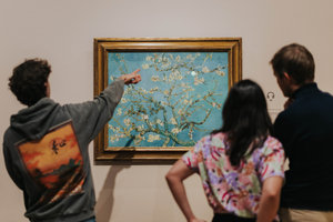 Een jongere wijst naar het schilderij Amandelbloesem van Vincent van Gogh in het Van Gogh Museum. Twee andere jongeren kijken toe. foto: Alicia Karsonopoero