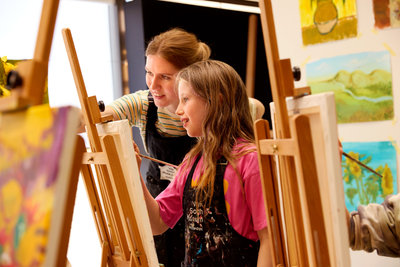 A girl is painting in the studio of the Van Gogh Museum while the workshop docent looks on with a friendly smile. Photo: Suzanne Karsters
