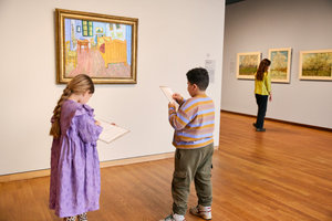 A girl and a boy stand in front of Vincent van Gogh's painting The Bedroom at the Van Gogh Museum and draw the painting. Photo: Suzanne Karsters