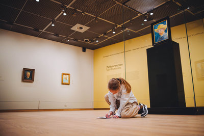 A child sits on the floor while participating in the treasure hunt at the self-portraits exhibition room. Photo: Jelle Draper.