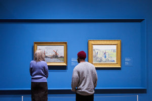 Two visitors look at Monet's work 'Windmills near Zaandam' in the exhibition 'Here to Stay'. Next to it hangs the painting 'Haymaking, Éragny' by Pissarro. Photo: Tomek Dersu Aaron