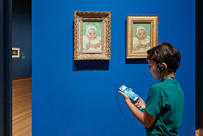 Een jongen luistert naar de audiotour bij de portretten van baby Marcelle Roulin in de tentoonstelling Van Gogh en de Roulins in het Van Gogh Museum. Foto: Michael Floor
