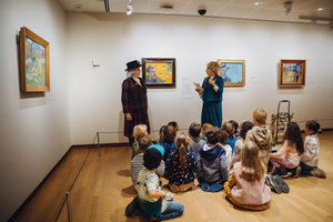 Schoolkinderen uit groep 1 en 2 zitten op de grond voor een zelfportret van Paul Gauguin in het Van Gogh Museum tijdens de theatrale rondleiding Famille van Camille. Foto: Jelle Draper