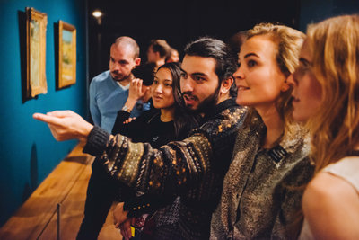 Een jongeman wijst naar een kunstwerk (buiten zicht). Twee jonge vrouwen luisteren aandachtig. Foto: Jelle Draper
