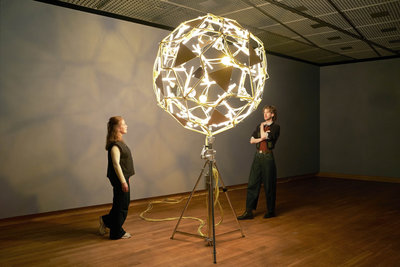 Twee bezoekers in de tentoonstelling 'Geel. Meer dan van Goghs lievelingskleur' kijken gefascineerd naar de installatie 'Who is afraid yellow flowerball' van Olafur Eliasson. Foto Michael Floor.