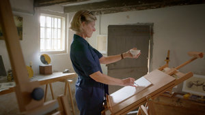 Videostill uit de tekensworkshop Teken het boerenleven. De workshopdocent tekent een kopje in haar hand na in Van Goghs atelier in Nuenen