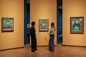 Twee bezoekers in de tentoonstelling van Gogh en de Roulins staan voor een schilderij van postbode Joseph Roulin en luisteren naar de audiotour in het Van Gogh Museum. Foto: Michael Floor