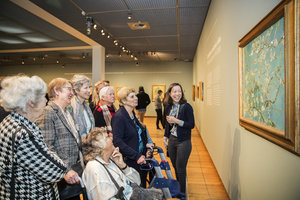 Een groep vrolijke oudere dames krijgt uitleg van een rondleider bij het schilderij Amandelbloesem van Vincent van Gogh. foto: Jessy fotografie & beeldbewerking