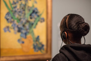 A girl is looking at Van Gogh's Irises painting while listening to the audio guide.
