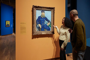 Twee bezoekers in de tentoonstelling van Gogh en de Roulins kijken naar een schilderij van postbode Joseph Roulin in het Van Gogh Museum. Foto: Michael Floor